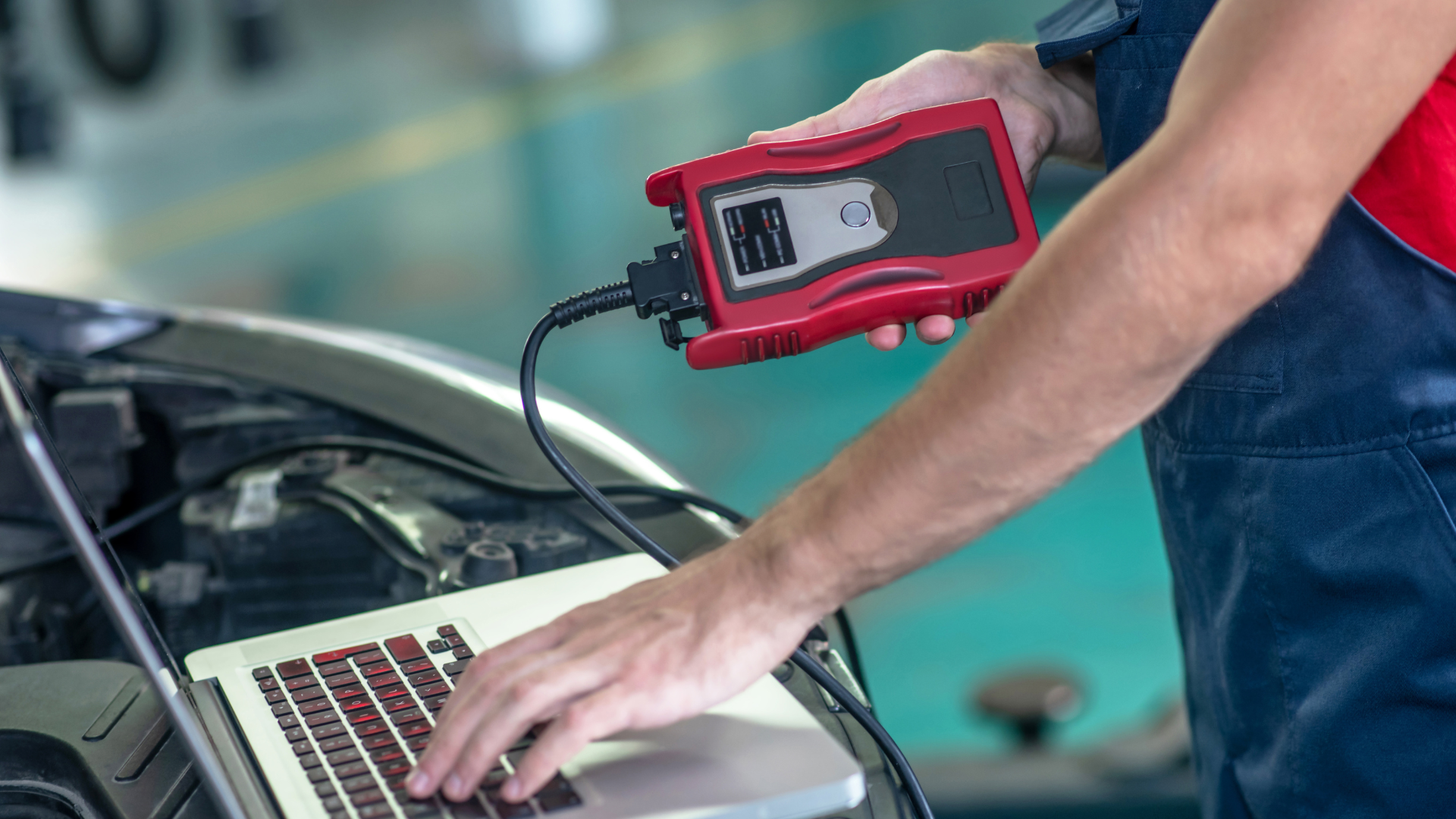 Mechanic using a diagnostic tool connected to a car and a laptop in a garage, analyzing data.