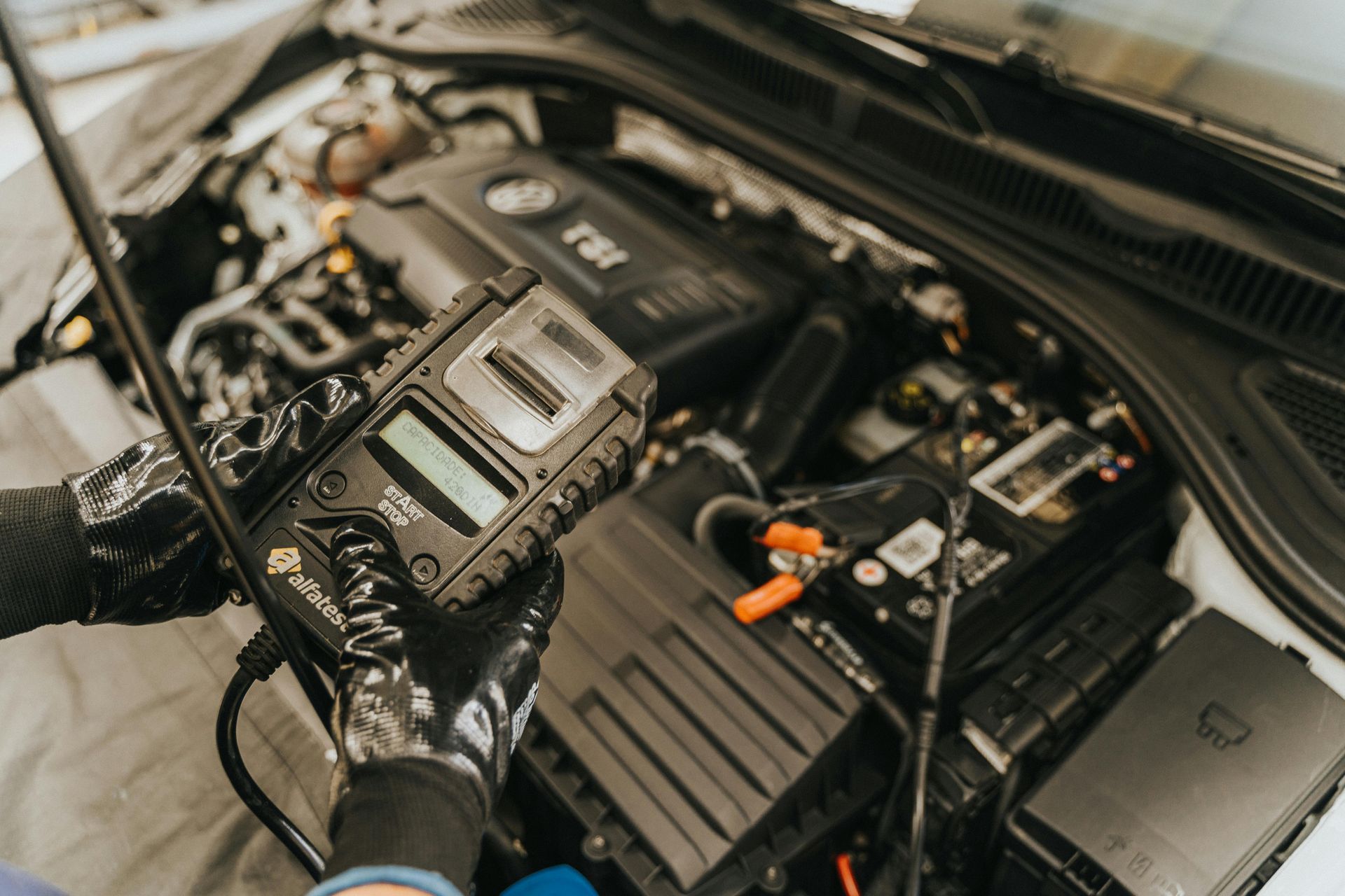 Mechanic using a diagnostic tool on a car engine. Black gloves, engine bay visible.