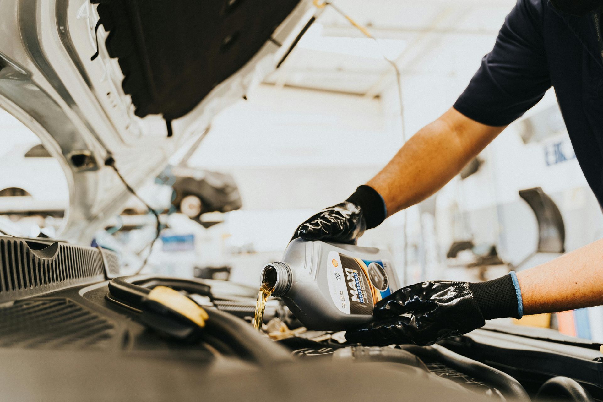 Mechanic pours oil into a car engine, hands in black gloves, in a garage.