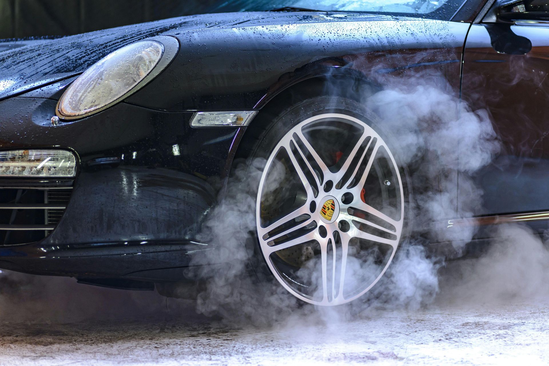 Black sports car doing a burnout, tires smoking.