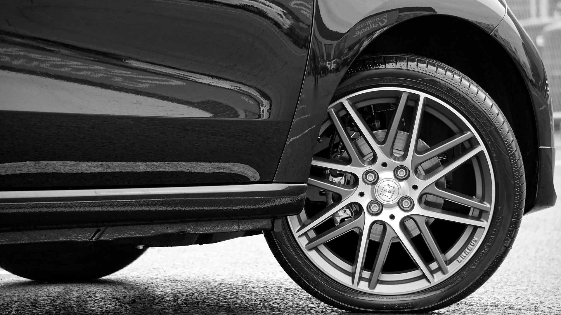 Black car tire and rim detail on wet asphalt.